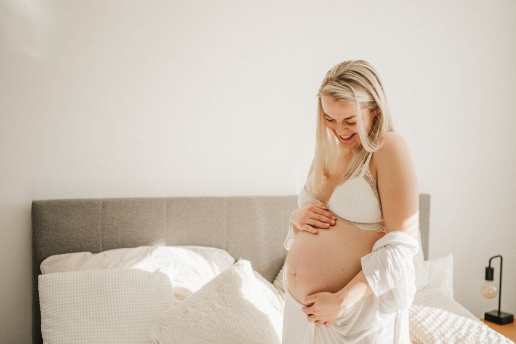 na těhotenském focení se směje těhotná žena a pózuje v posteli a v županu-fotografka Veronika Kovačková-Žďár nad Sázavou-Vysočina
